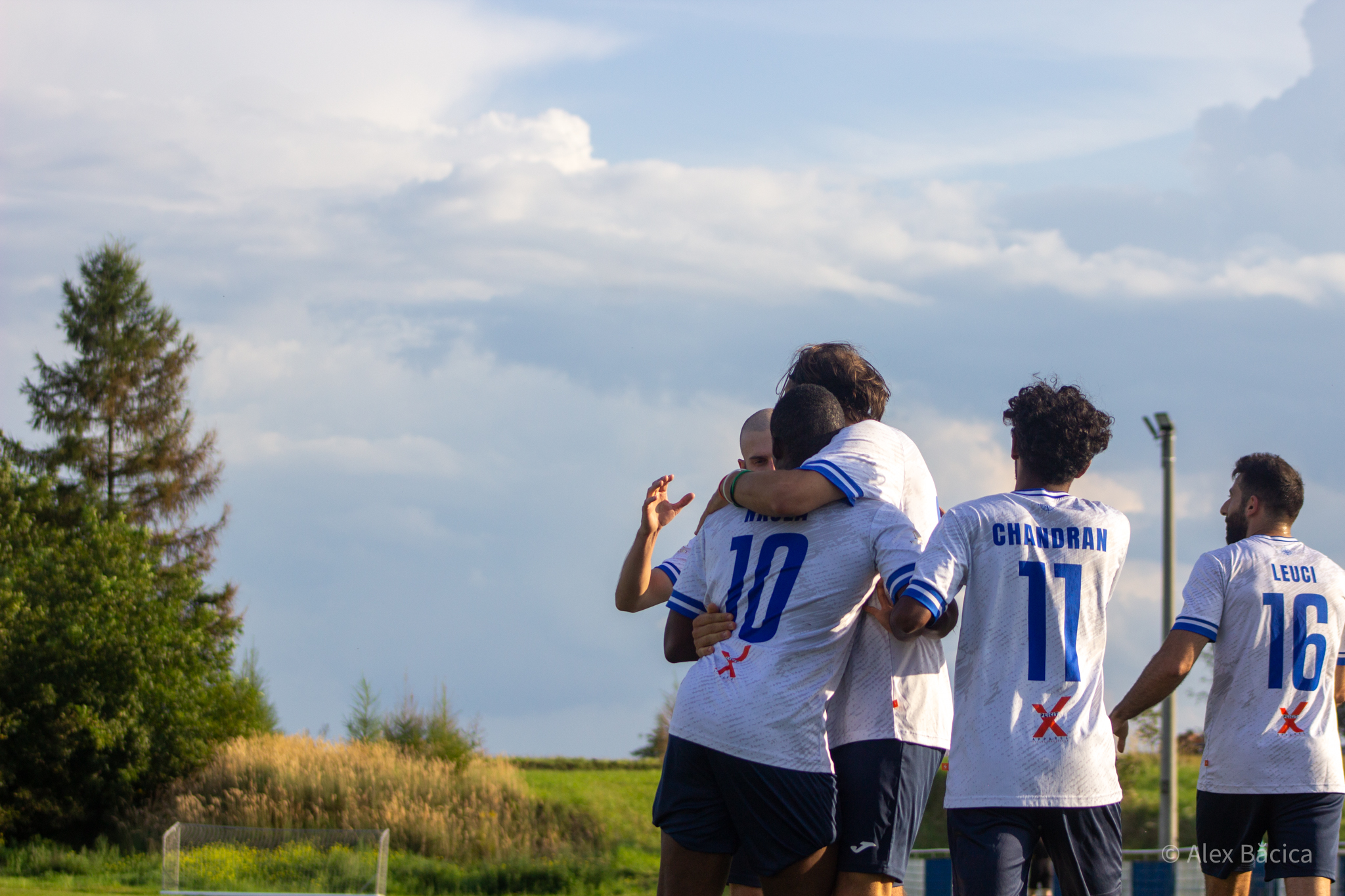 Players of Krakow Dragoons FC celebrating a goal with a nice view of a corn field and a dramatic sky in the background