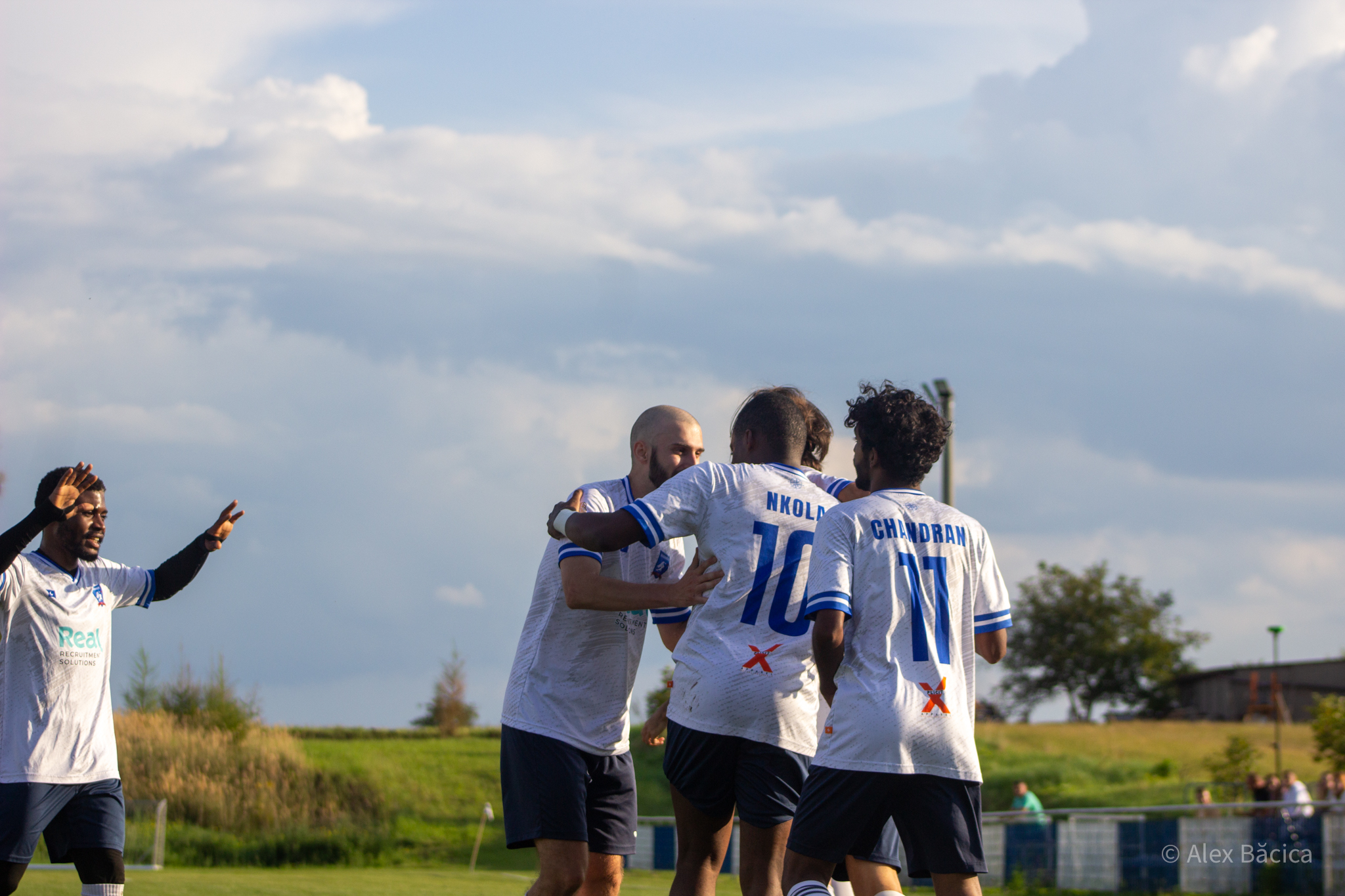 Players of Krakow Dragoons FC celebrating a goal with a nice view of a corn field and a dramatic sky in the background